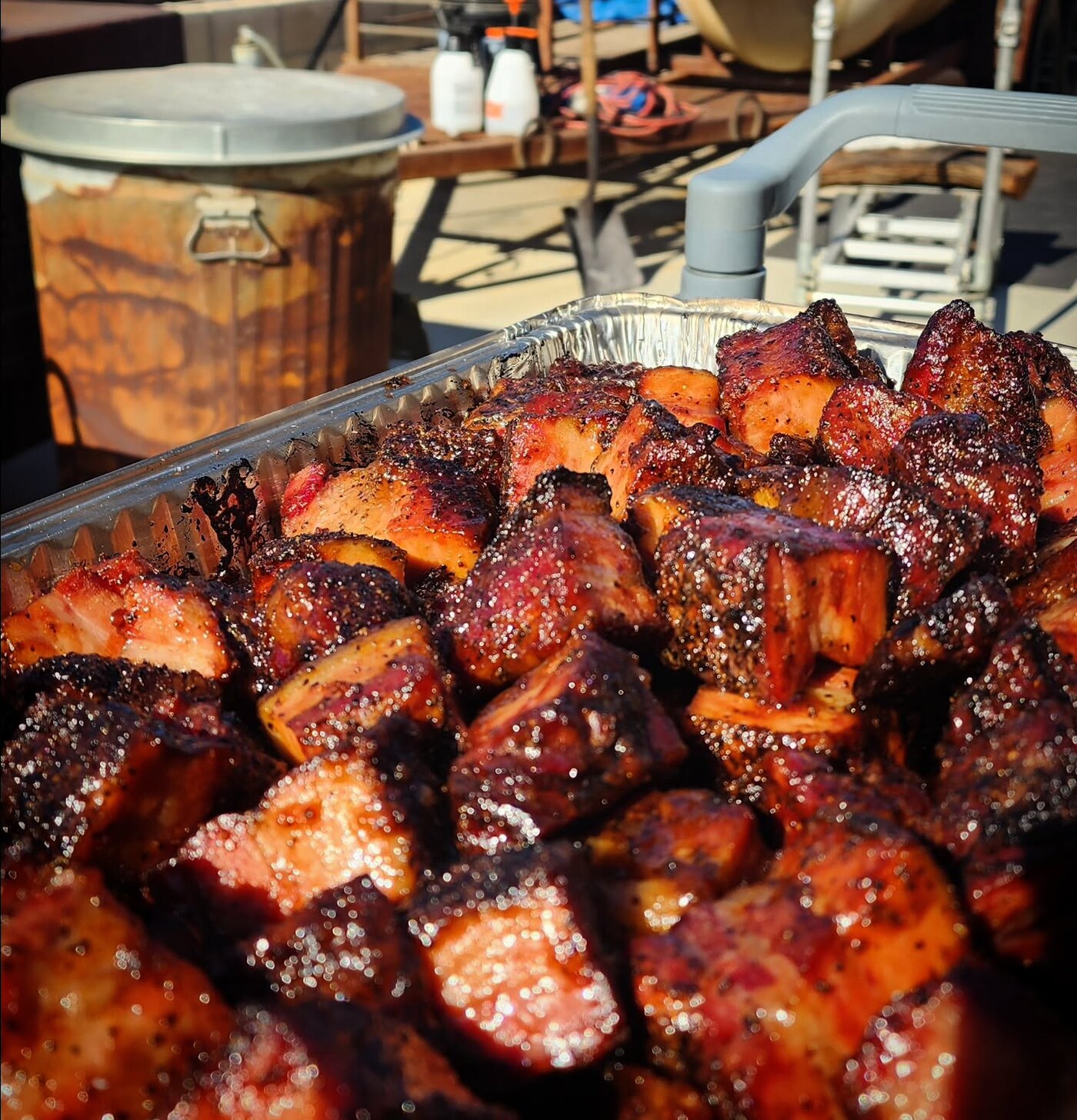 Pork belly burnt ends glistening in a tray beside the smoker
