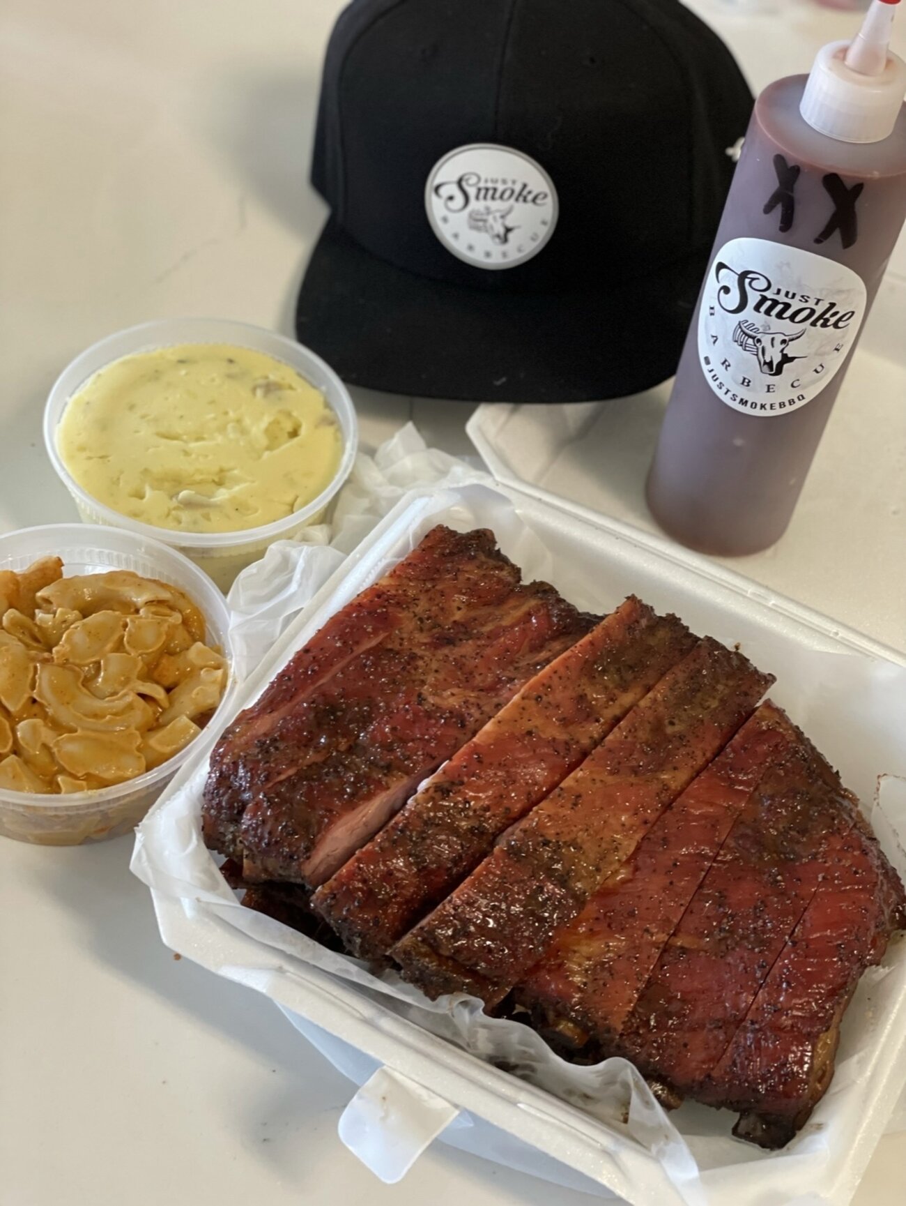 A rack of spare ribs boxed with mac and cheese and a house sauce bottle