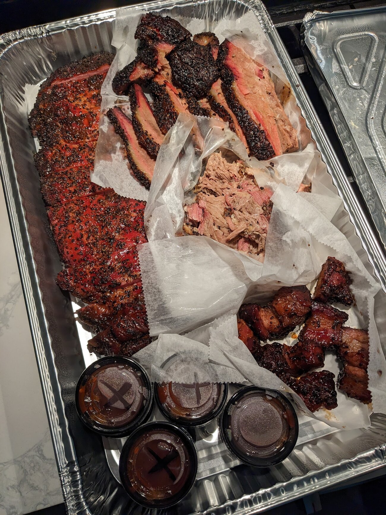 A tray of brisket and ribs with sauce cups